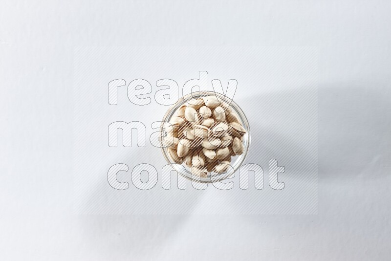 A glass bowl full of pistachios on a white background in different angles