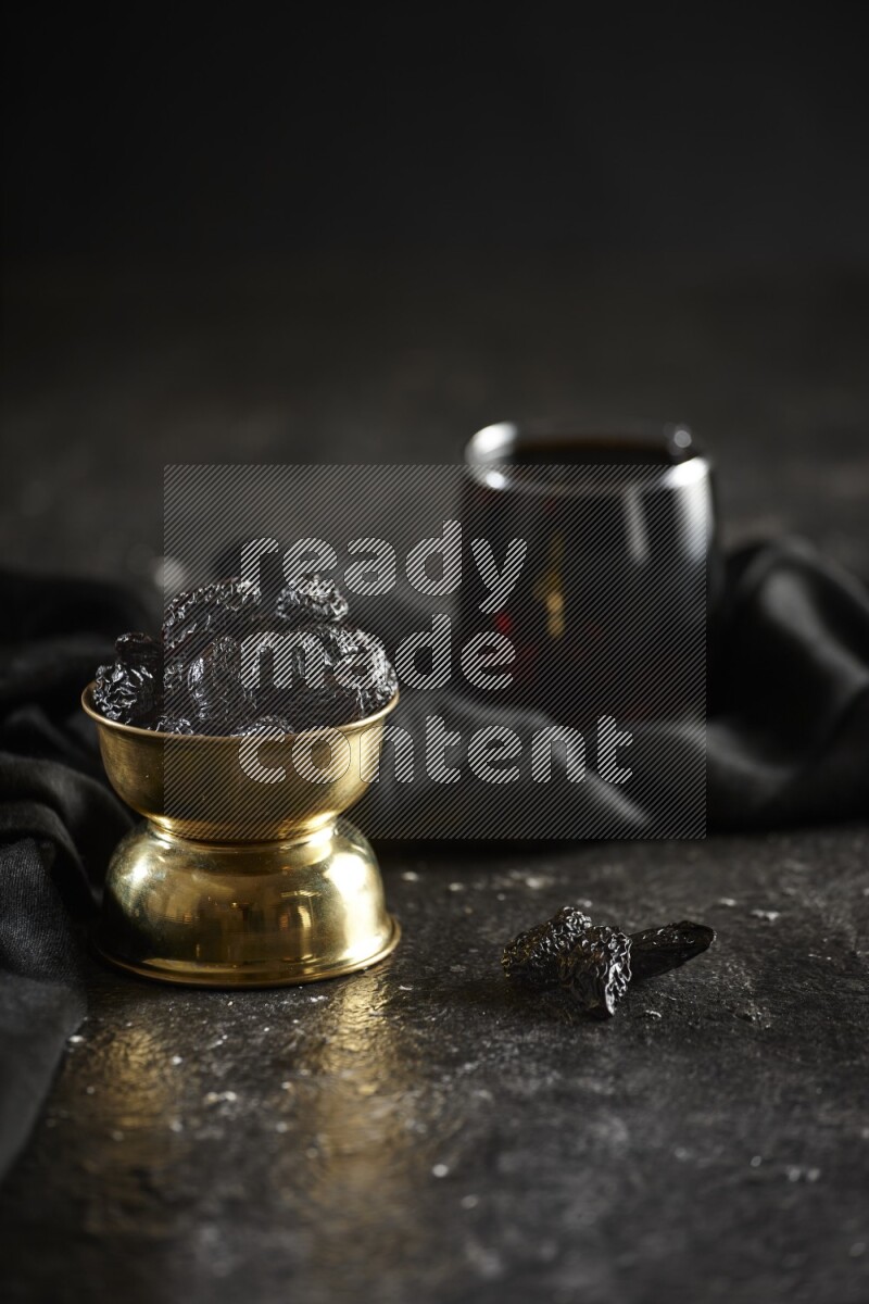 Dried fruits in a metal bowl with tamarind and a napkin in a dark setup