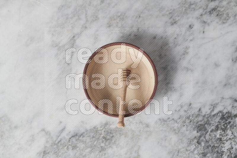 Beige pottery oven plate with wooden honey dipper in it on grey marble background