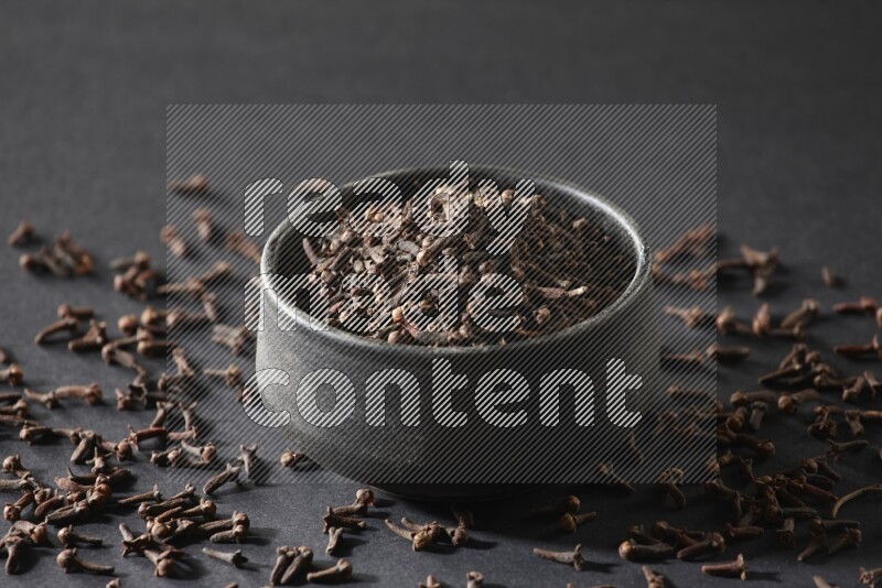 A black pottery bowl full of cloves on a black flooring