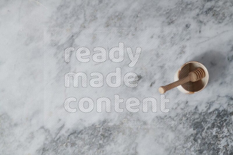 وعاء فخاري متعدد الألوان مع ملعقة عسل خشبية بداخله على خلفية من الرخام الرمادي