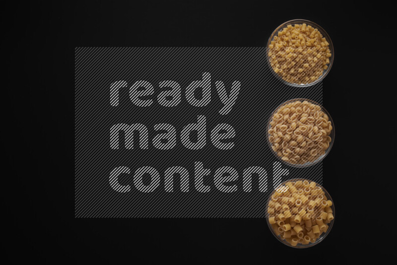 Different pasta types in 3 glass bowls on black background