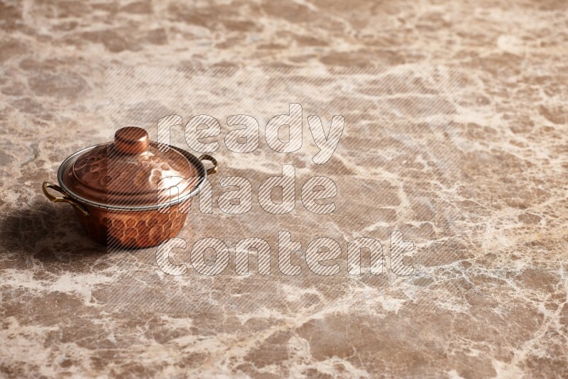 A small copper pot on beige marble background