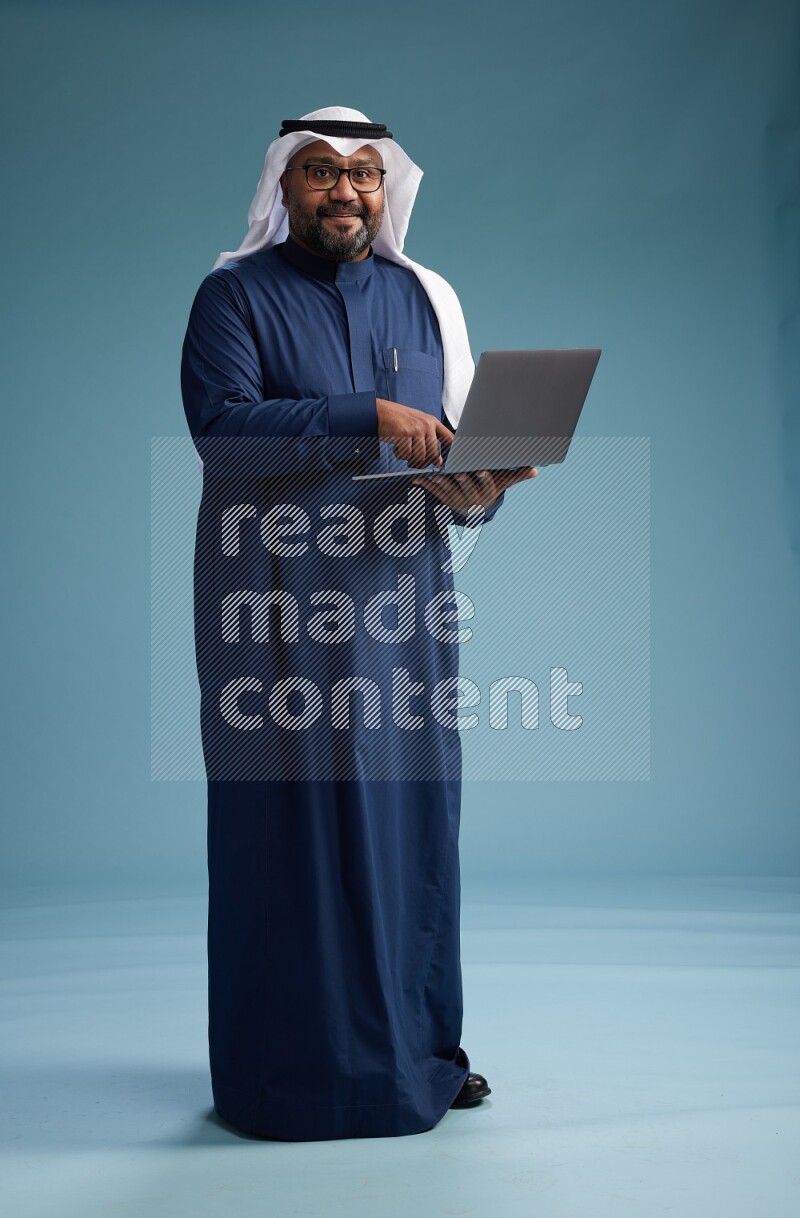 Saudi Man with shimag Standing working on laptop on blue background