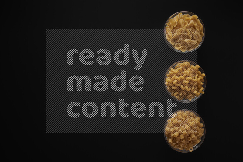Different pasta types in 3 glass bowls on black background