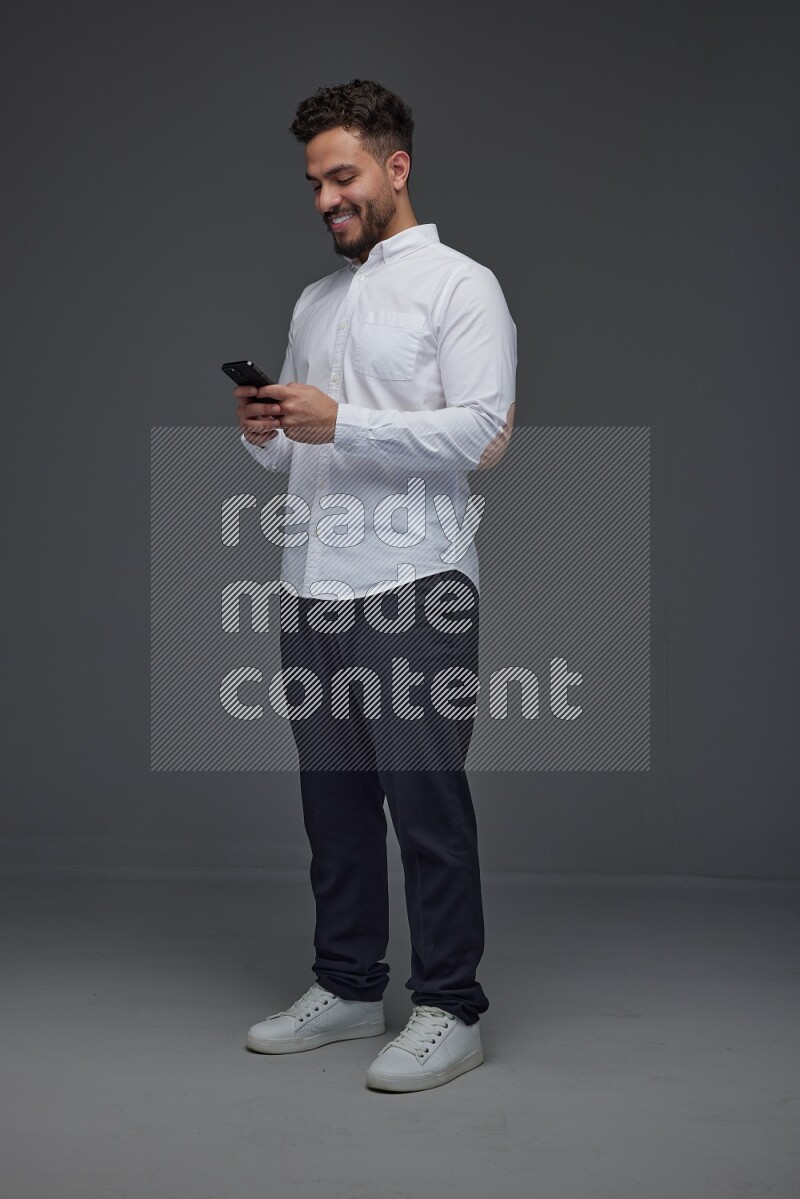 A man wearing smart casual standing and using his phone eye level on a gray background