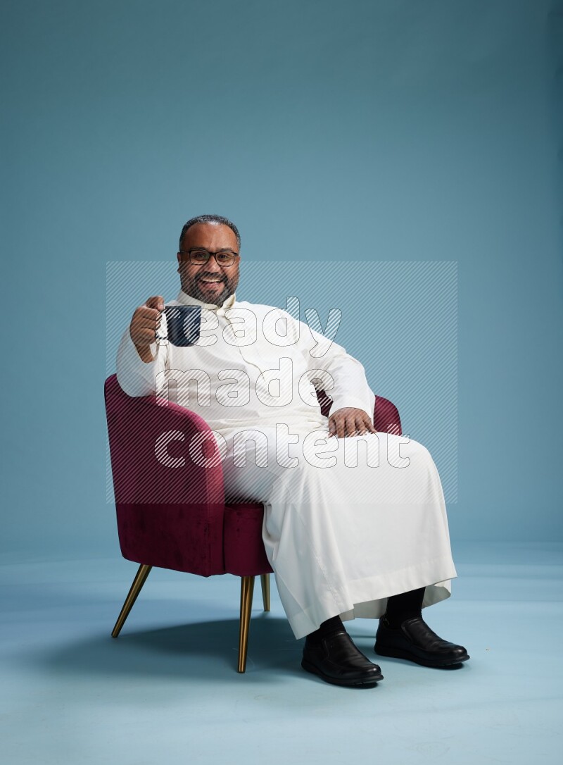 Saudi Man without shimag sitting on chair drinking coffee on blue background