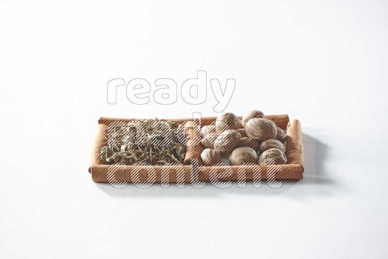 مربعان من أعواد القرفة ممتلئان بالريحان المجفف وجوزة الطيب علي خلفية بيضاء