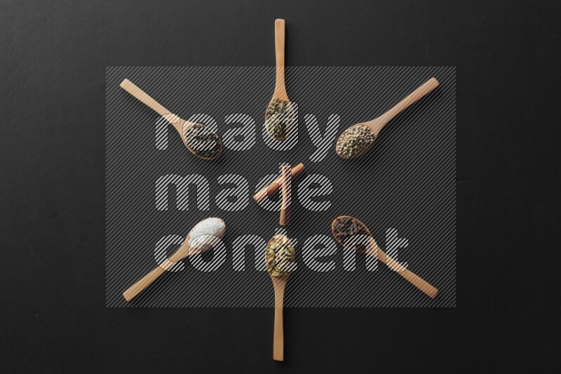 wooden spoons filled with white peppers, cloves, cardamom, salt, black peppers and basil on black flooring and shaped like a clock