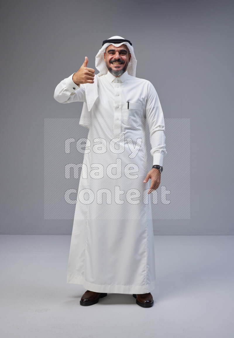 Saudi man Wearing Thob and white Shomag standing interacting with the camera on Gray background