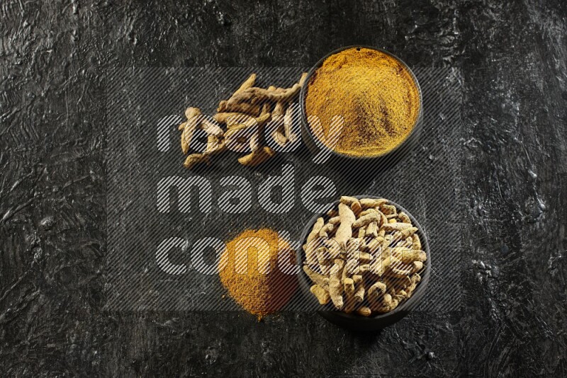 وعاءان من الفخار باللون الأسود، أحدهما ممتلئ ببودرة الكركم والآخر ممتلئ بأصابع كاملة من الكركم المجفف على خلفية سوداء