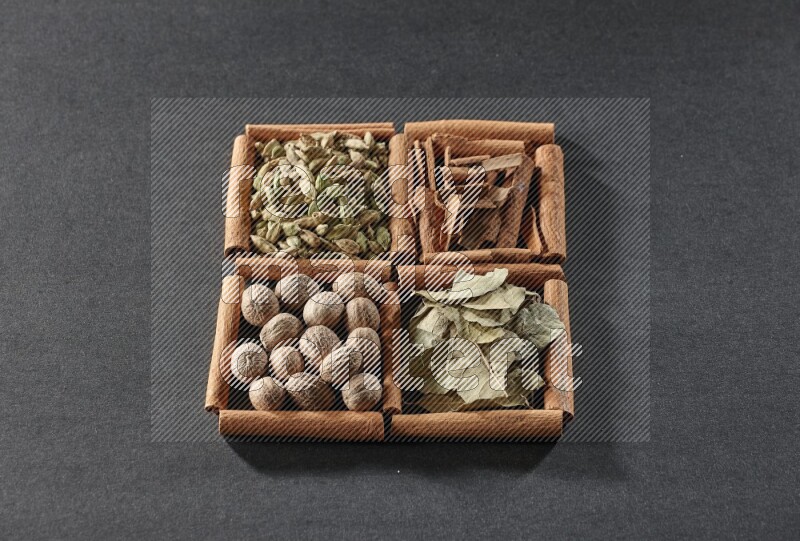 4 مربعات من عيدان القرفة ممتلئة بقطع القرفة وحبوب الهيل وأوراق الغار وجوزة الطيب على أرضية سوداء