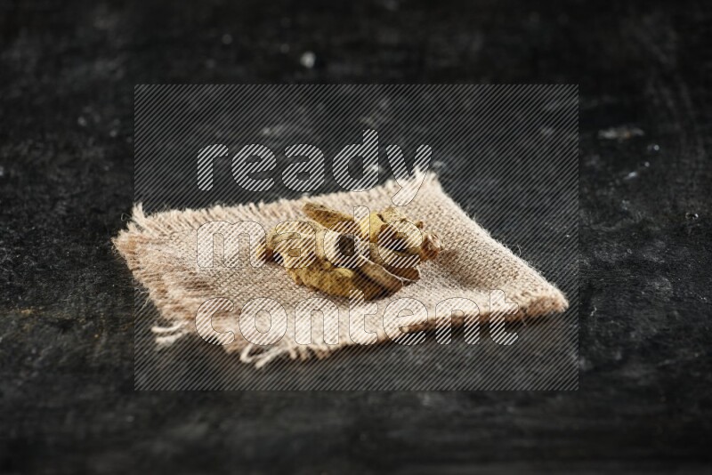 Dried turmeric whole fingers on a burlap piece of fabric on textured black flooring