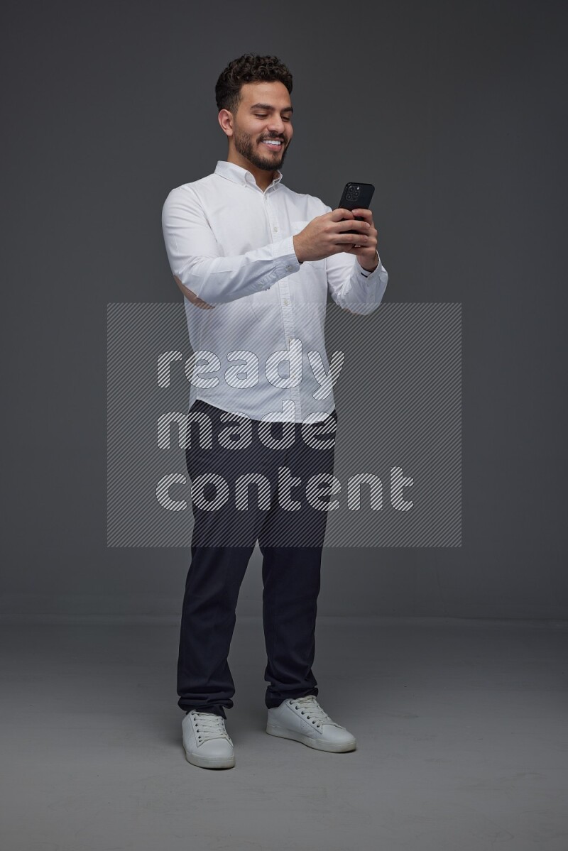 A man wearing smart casual standing and using his phone eye level on a gray background