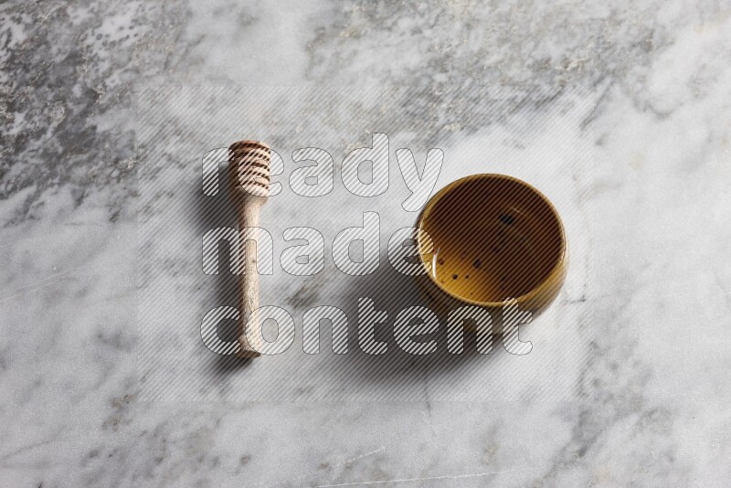 Multicolored pottery bowl with wooden honey dipper on the side on grey marble background