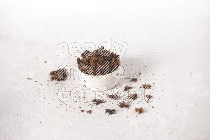 Star Anise in a white bowl and more of it sprinkled on white background