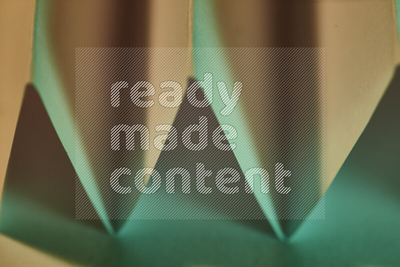 A close-up abstract image showing sharp geometric paper folds in green gradients and warm tones