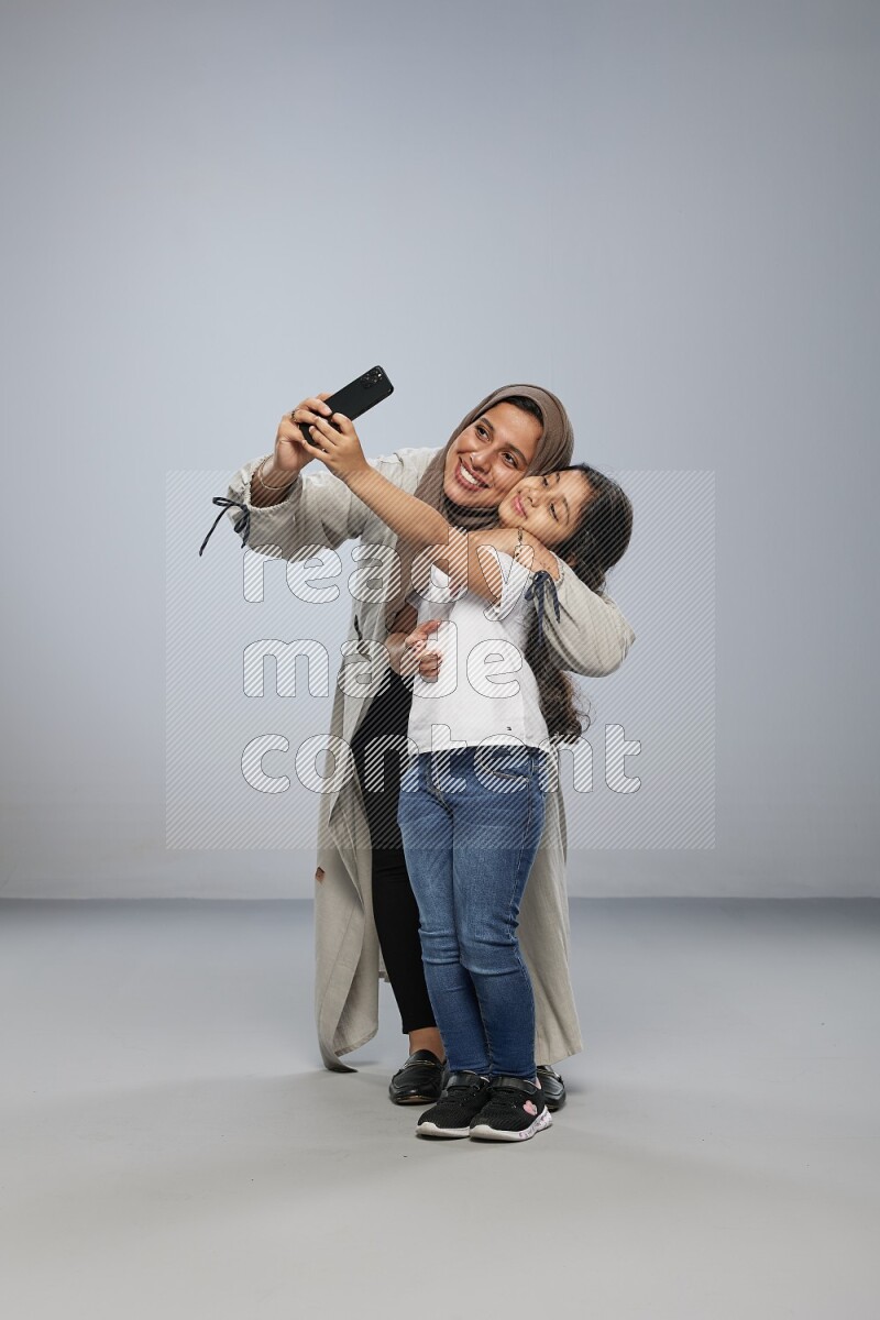 A girl standing taking selfie with her mother on gray background