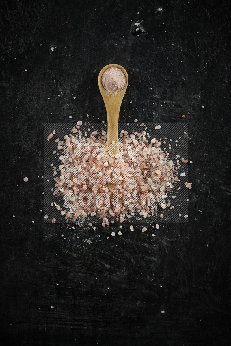 A wooden spoon full of pink himalayan salt on black background