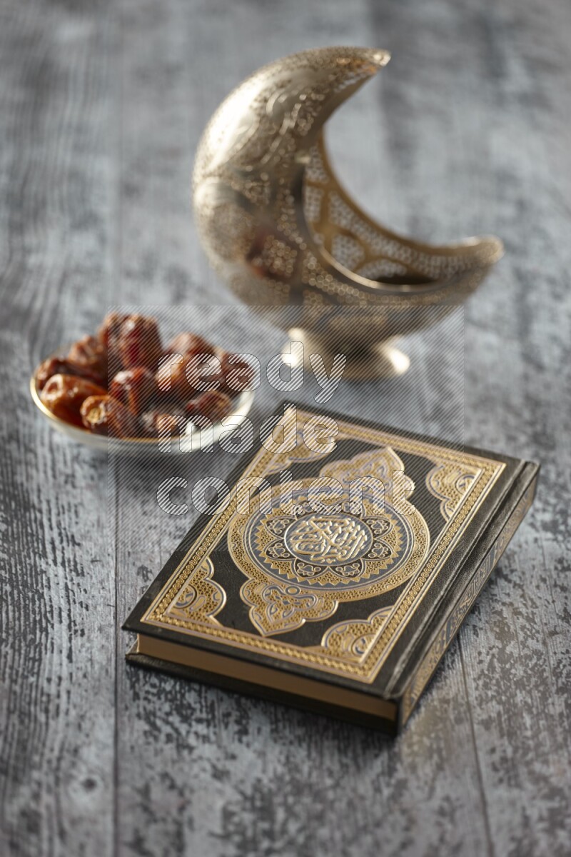 A silver lantern with different drinks, dates, nuts, prayer beads and quran on grey wooden background