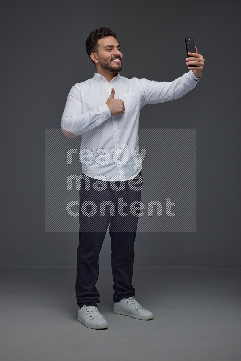 A man wearing smart casual and taking selfie with his phone eye level on a gray background