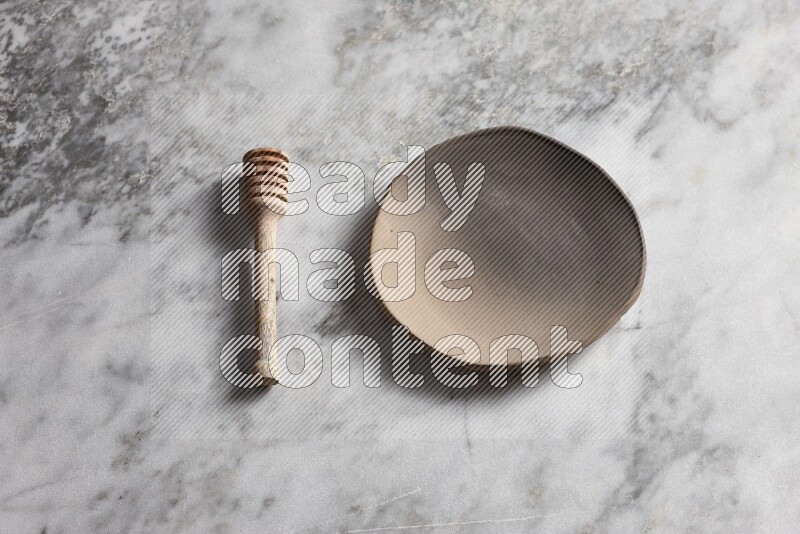Multicolored pottery plate with wooden honey dipper on the side on grey marble background