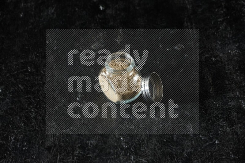 وعاء زجاجي للتوابل ممتلئ ببودرة الهيل على خلفية سوداء