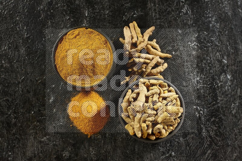 وعاءان من الفخار باللون الأسود، أحدهما ممتلئ ببودرة الكركم والآخر ممتلئ بأصابع كاملة من الكركم المجفف على خلفية سوداء