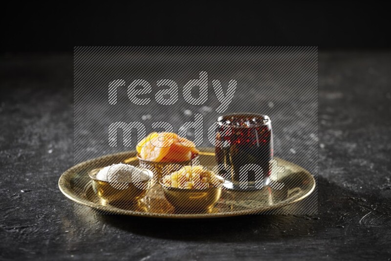 Dried fruits in metal bowls with tamarind on a tray in dark setup