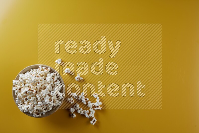 A multicolored ceramic plate full of popcorn with popcorn beside it on a yellow background in different angles