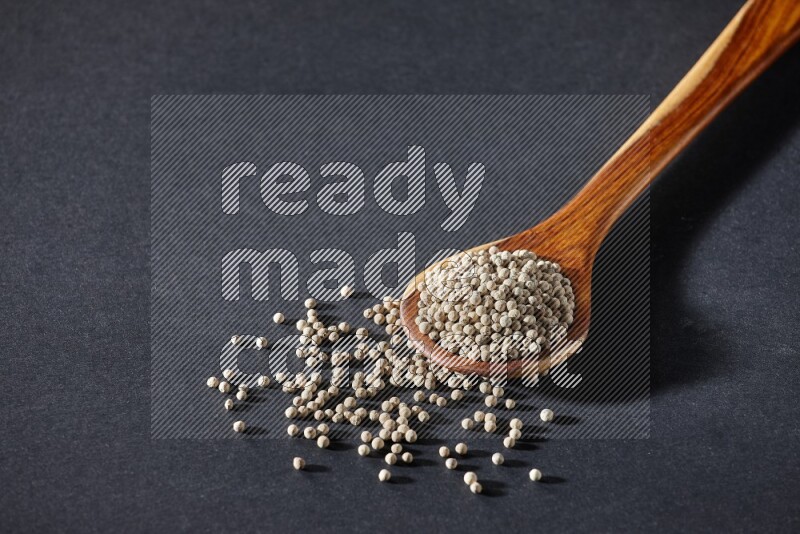 A wooden ladle full of white pepper beads on black flooring