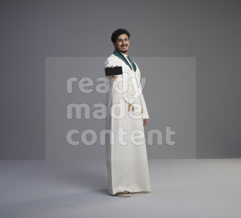 رجل سعودي يرتدي ثوب ابيض و شال يحمل جوال