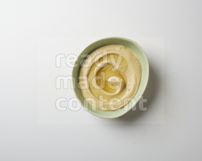 Hummus in a green plate garnished with olive oil on a white background