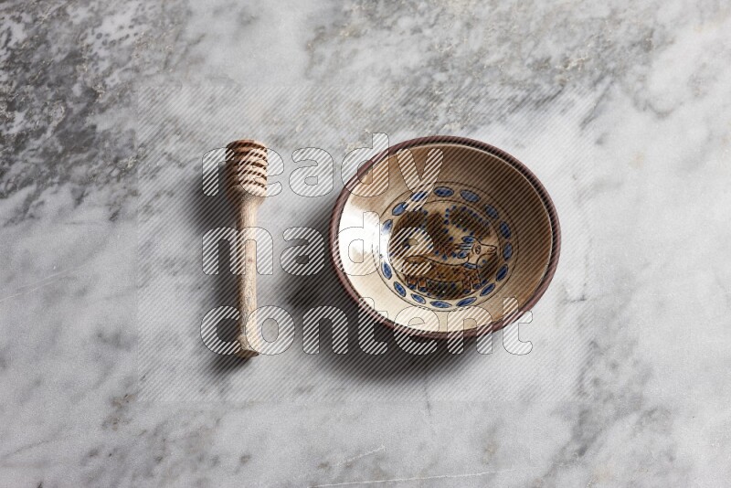 Decorative pottery plate with wooden honey dipper on the side on grey marble background