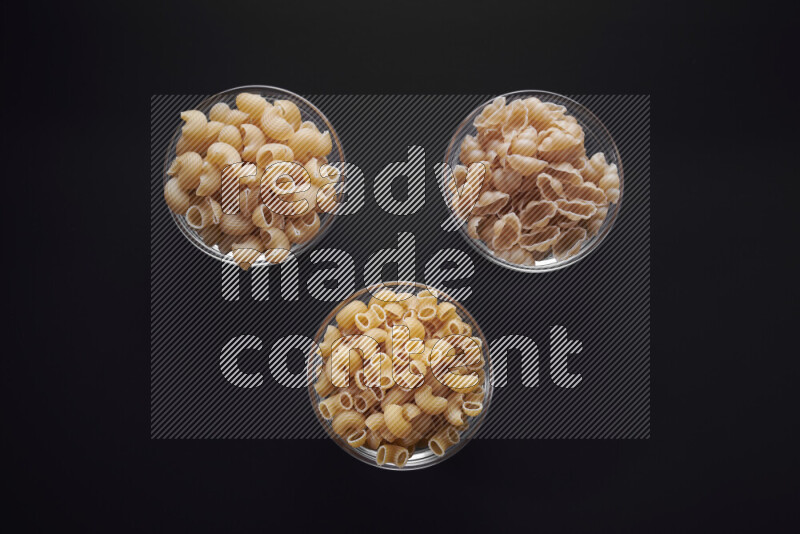 Different pasta types in glass bowls on black background