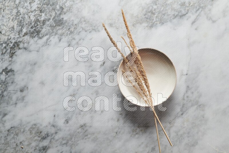 Wheat stalks on beige pottery plate on grey marble background