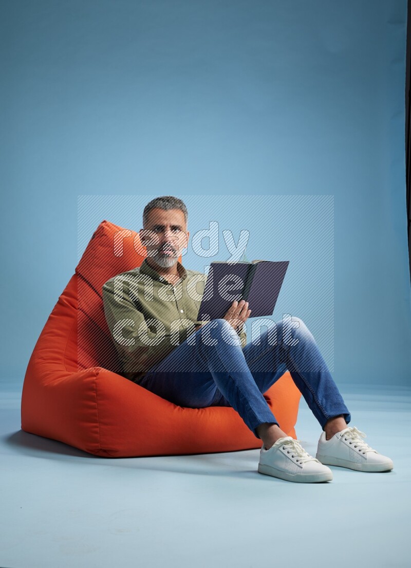 A man sitting on an orange beanbag and reading a book