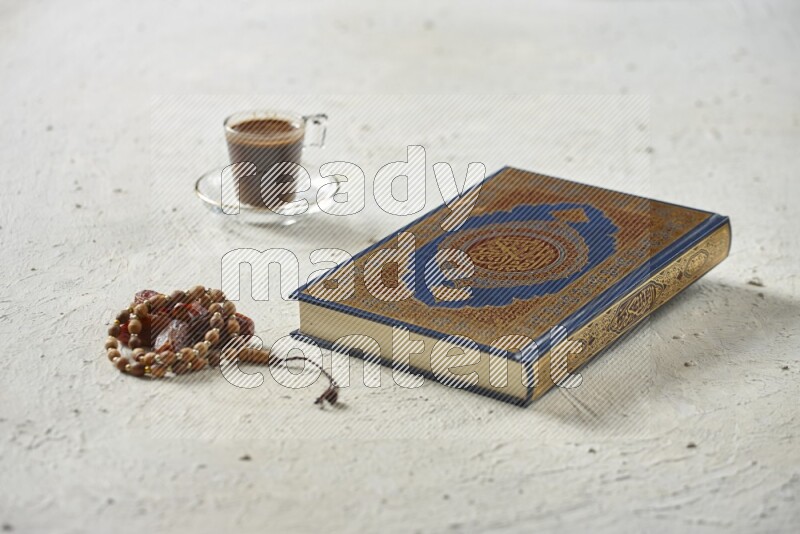Quran with dates, prayer beads and different drinks all placed on textured white background