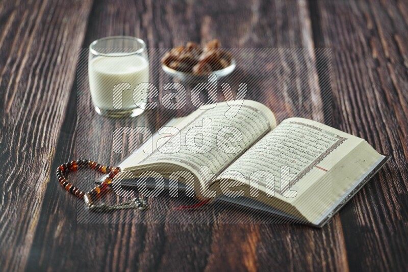 Quran with dates, prayer beads and different drinks all placed on wooden background