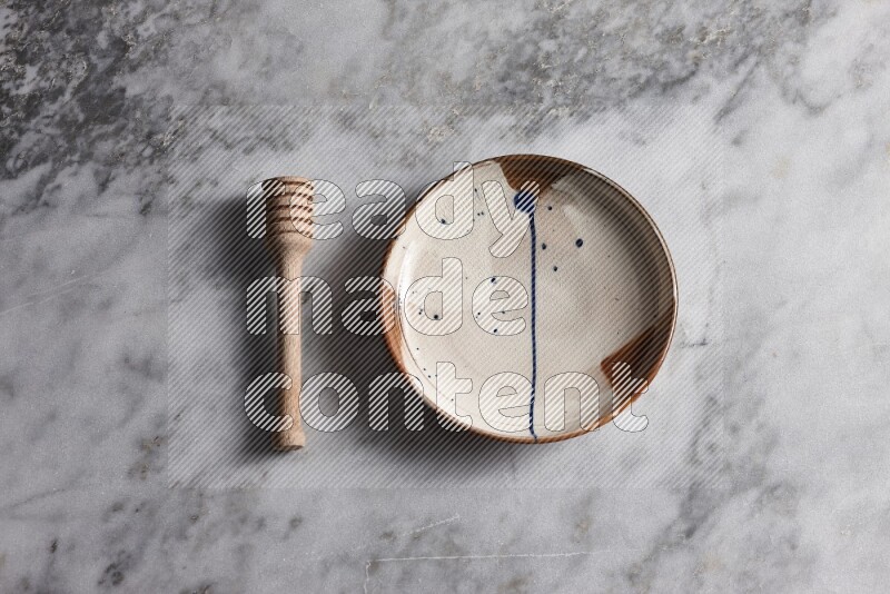 Multicolored pottery plate with wooden honey dipper on the side on grey marble background