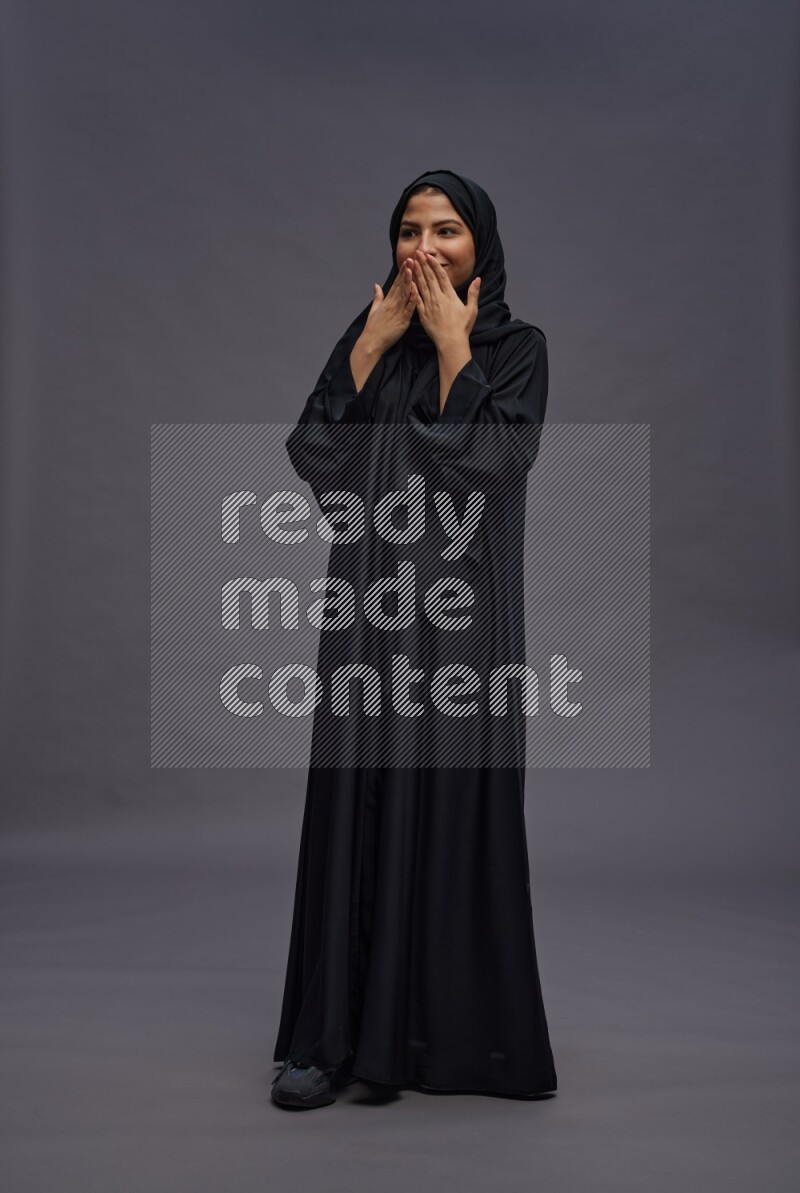 Saudi woman wearing Abaya standing hands behind head on gray background