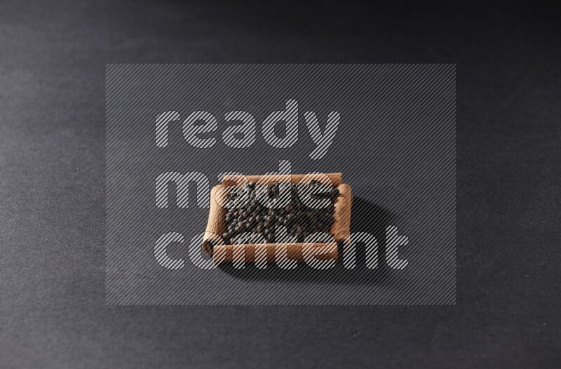 A single square of cinnamon sticks full of black pepper on black flooring