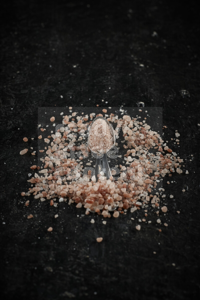 2 metal spoons filled with pink himalayan salt on black background