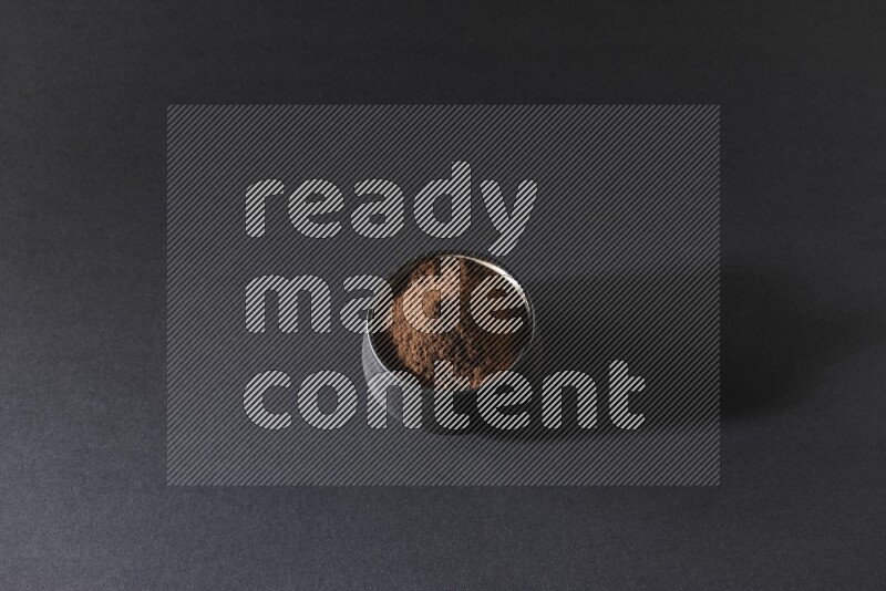 A black pottery bowl full of cloves powder on a black flooring