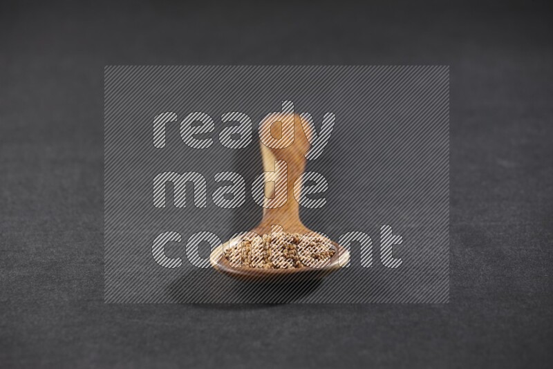 A wooden spoon full of mustard seeds on a black flooring