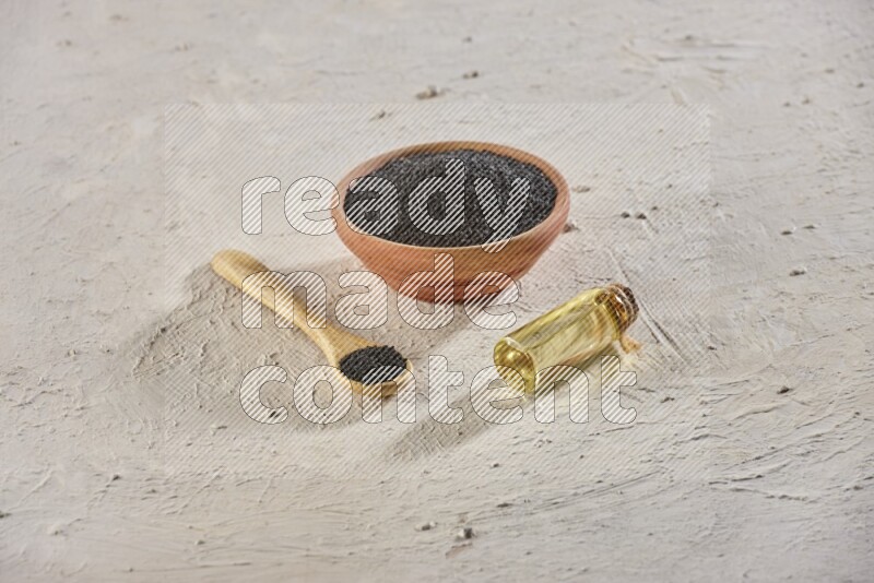 وعاء خشبي وملعقة مليئان ببذور حبة البركة مع زجاجة من زيت حبة البركة على أرضية بيضاء