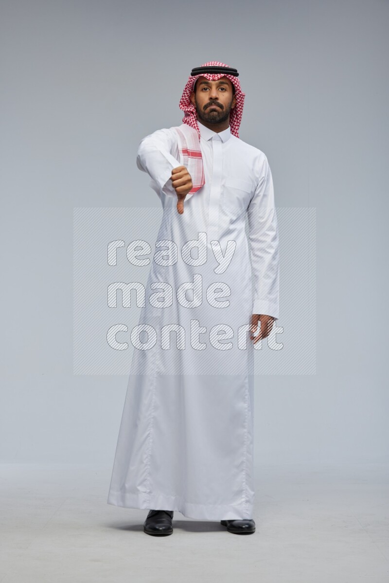 Saudi man Wearing Thob and shomag standing interacting with the camera on Gray background