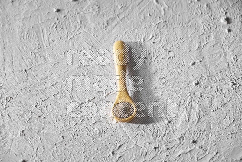 A wooden spoon full of black pepper powder on a textured white flooring