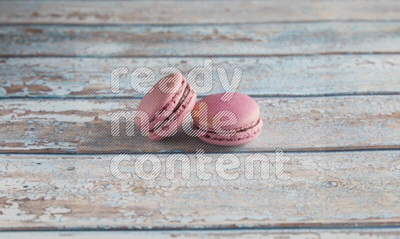 45º Shot of two Purple Strawberry macarons on light blue wooden background