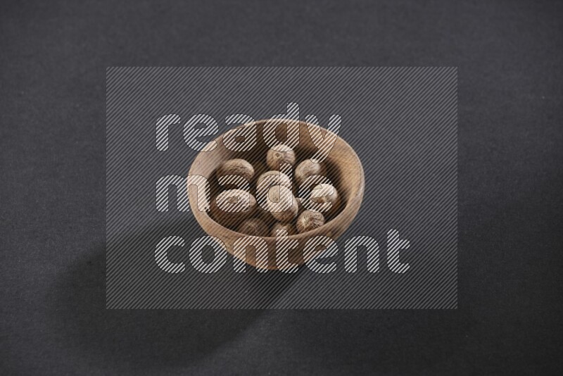 A wooden bowl full of whole nutmeg seeds on a black flooring